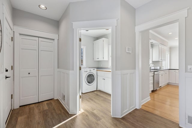 laundry room with cabinet space, a wainscoted wall, a sink, and washer / dryer