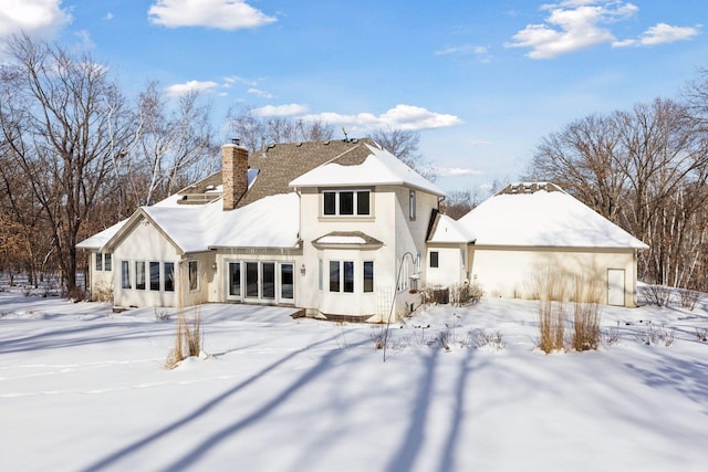 snow covered rear of property with a garage and a chimney