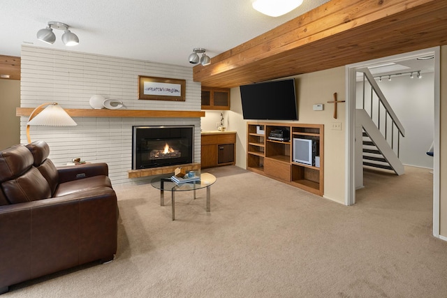 carpeted living area featuring a brick fireplace, stairs, and rail lighting