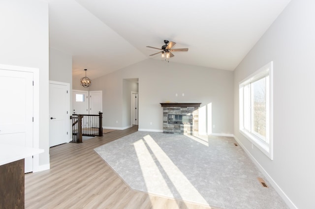 unfurnished living room featuring lofted ceiling, a stone fireplace, ceiling fan with notable chandelier, and light hardwood / wood-style floors