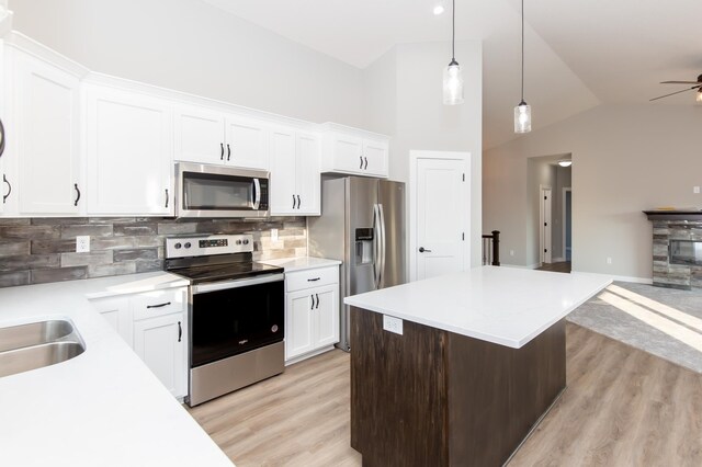 kitchen featuring white cabinetry, appliances with stainless steel finishes, decorative light fixtures, and vaulted ceiling