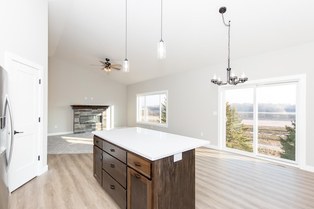 kitchen featuring hanging light fixtures, dark brown cabinets, light hardwood / wood-style floors, a stone fireplace, and vaulted ceiling