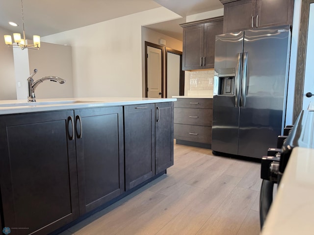 kitchen featuring pendant lighting, sink, backsplash, stainless steel fridge with ice dispenser, and light wood-type flooring