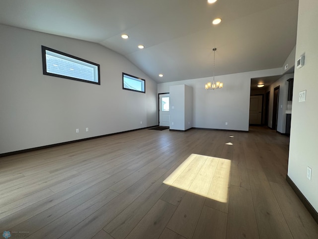 empty room with lofted ceiling, plenty of natural light, an inviting chandelier, and light hardwood / wood-style floors