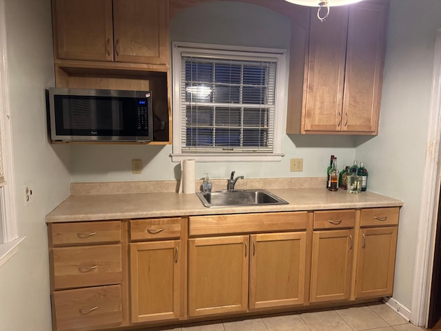 kitchen featuring stainless steel microwave, light tile patterned flooring, light countertops, and a sink