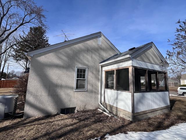 view of side of property featuring a sunroom, fence, central AC, and stucco siding