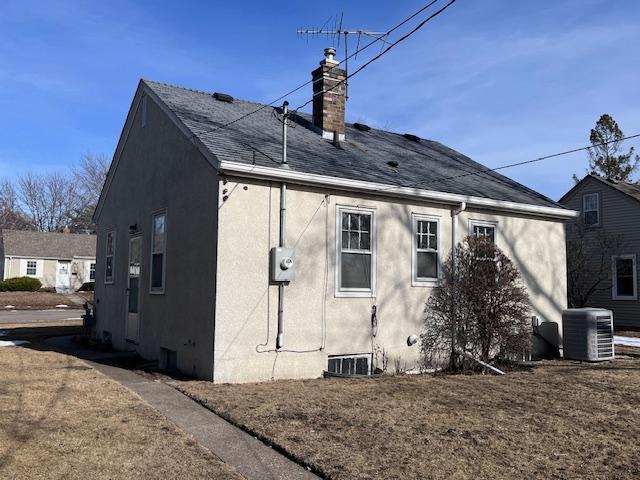 back of property featuring stucco siding, roof with shingles, central AC, and a chimney