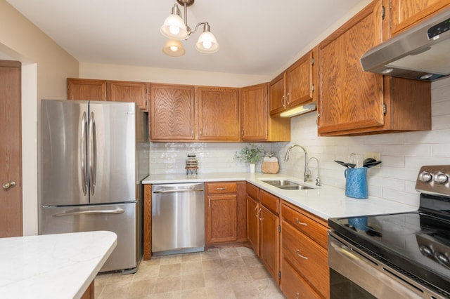 kitchen with a sink, light countertops, under cabinet range hood, appliances with stainless steel finishes, and backsplash