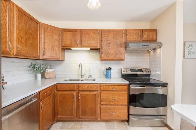 kitchen with brown cabinetry, stainless steel appliances, a sink, light countertops, and under cabinet range hood