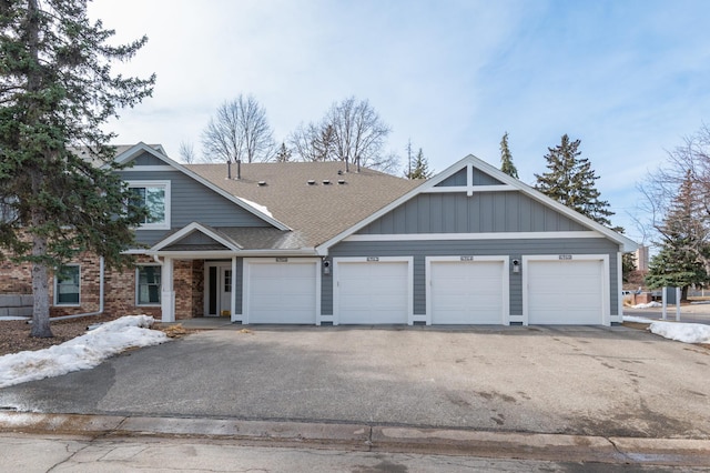 view of front of home with driveway, brick siding, and roof with shingles