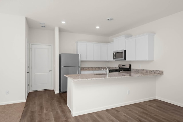 kitchen with appliances with stainless steel finishes, sink, white cabinets, kitchen peninsula, and light stone countertops