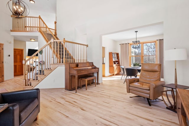 sitting room with a towering ceiling, light wood-style floors, stairway, and a chandelier