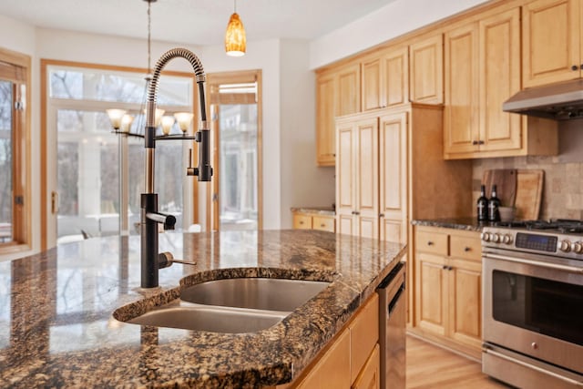 kitchen with pendant lighting, stainless steel appliances, a sink, dark stone countertops, and under cabinet range hood