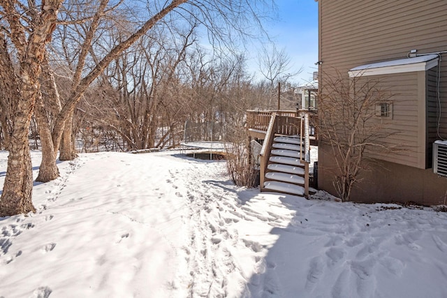 yard layered in snow with stairs, a trampoline, and a deck