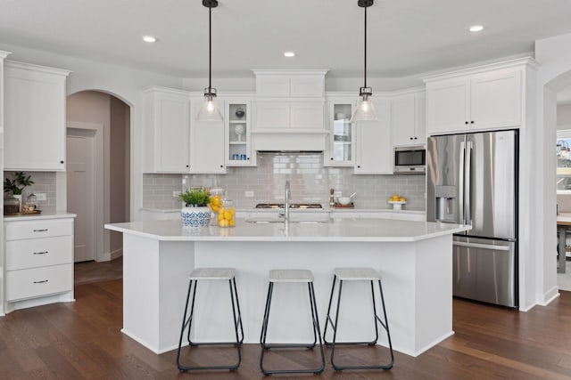 kitchen featuring stainless steel appliances, an island with sink, hanging light fixtures, and white cabinets