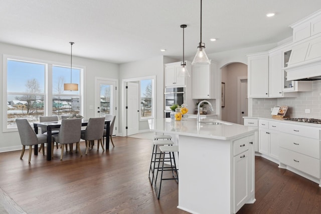 kitchen with a kitchen island with sink, sink, white cabinets, and decorative light fixtures