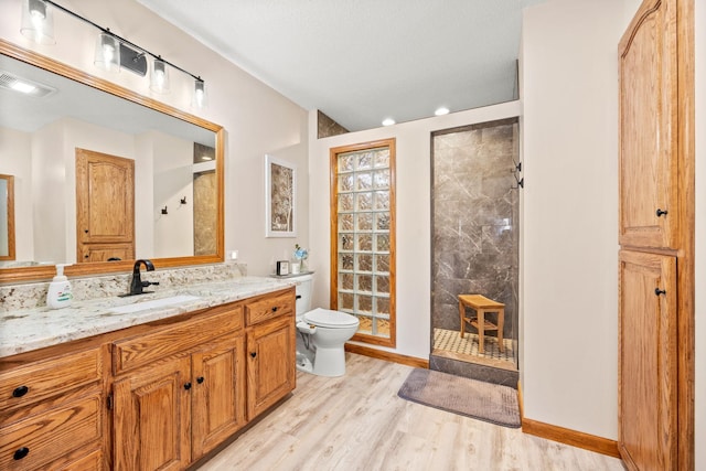 bathroom featuring toilet, tiled shower, vanity, and hardwood / wood-style flooring