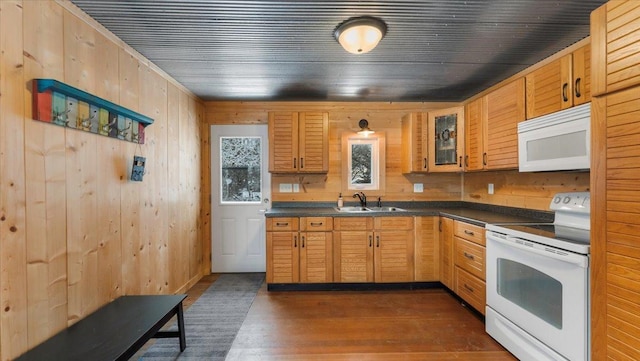 kitchen featuring white appliances, a sink, dark countertops, dark wood finished floors, and glass insert cabinets