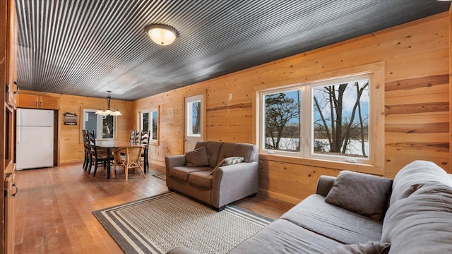 living room featuring wood walls, light wood finished floors, and an inviting chandelier