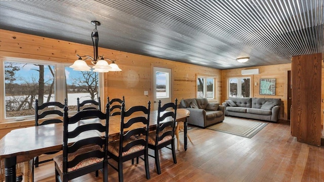 dining room featuring wood walls, a notable chandelier, a wall mounted AC, and wood finished floors