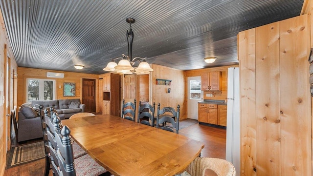 dining space with a chandelier, dark wood-style flooring, wood walls, and a wealth of natural light