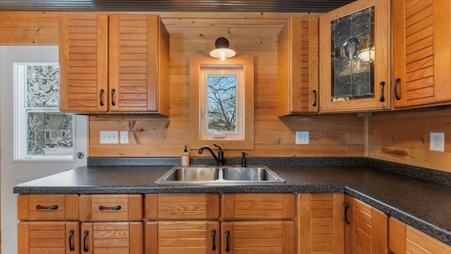 kitchen with dark countertops, glass insert cabinets, brown cabinets, and a sink