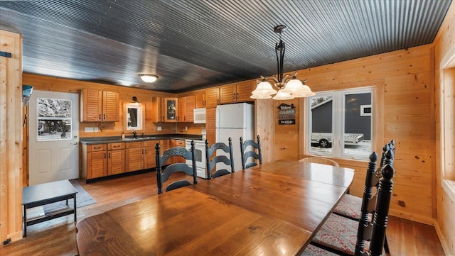 dining room with wooden walls, an inviting chandelier, and light wood-style floors