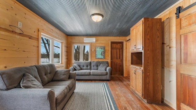 living room with wood walls, a barn door, light wood finished floors, and an AC wall unit