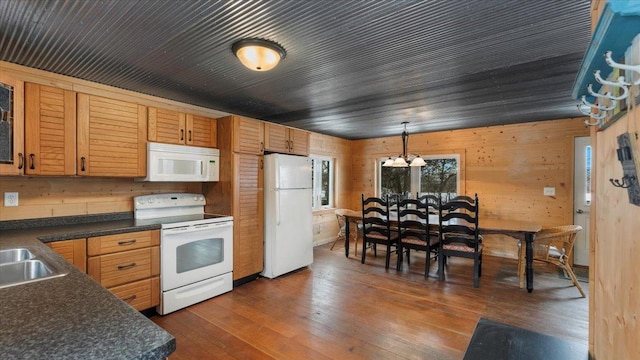 kitchen with hanging light fixtures, white appliances, dark countertops, and dark wood finished floors