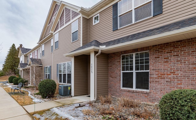 view of home's exterior featuring cooling unit, brick siding, and roof with shingles