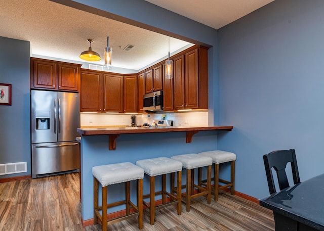 kitchen featuring stainless steel appliances, tasteful backsplash, visible vents, and wood finished floors