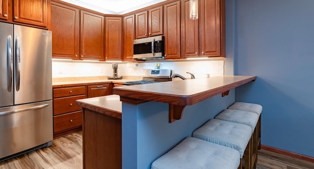 kitchen with tasteful backsplash, appliances with stainless steel finishes, a kitchen breakfast bar, a peninsula, and light wood-style floors