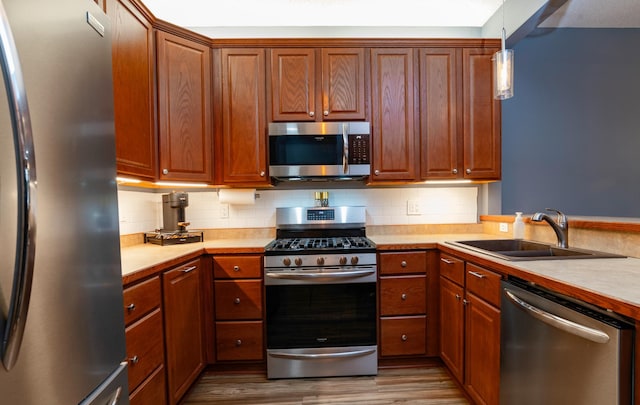 kitchen with stainless steel appliances, light countertops, a sink, and wood finished floors