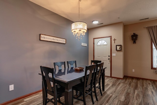 dining area featuring a chandelier, visible vents, baseboards, and wood finished floors