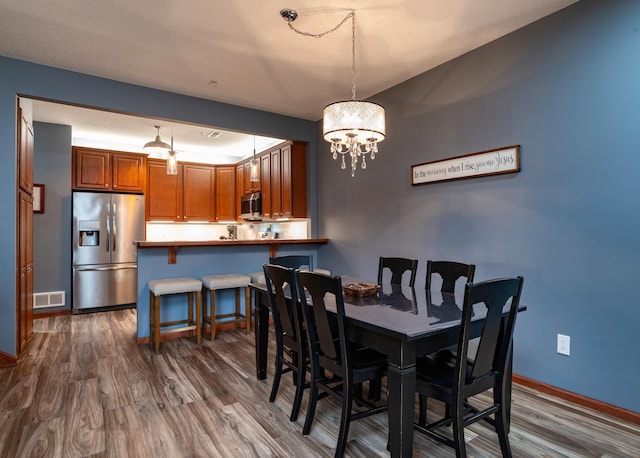 dining space with an inviting chandelier, visible vents, baseboards, and wood finished floors