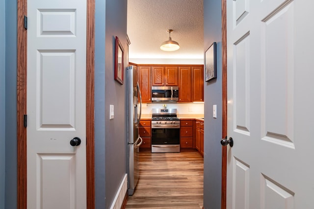 kitchen with brown cabinets, light wood-style flooring, stainless steel appliances, and a textured ceiling