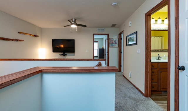 interior space with carpet flooring, a sink, baseboards, visible vents, and a ceiling fan