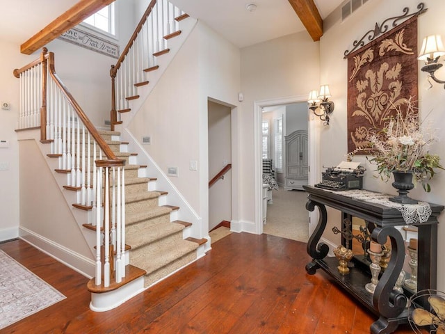 foyer featuring visible vents, hardwood / wood-style floors, beam ceiling, and baseboards