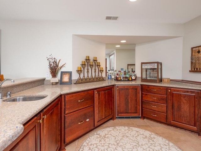 kitchen with light tile patterned floors, light stone counters, a peninsula, a sink, and visible vents