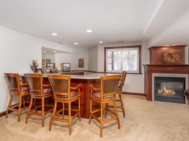 bar with recessed lighting, light colored carpet, baseboards, a bar, and a glass covered fireplace