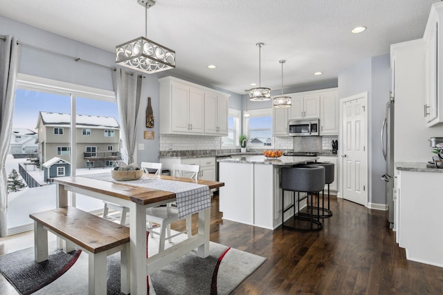 kitchen with white cabinets, appliances with stainless steel finishes, a kitchen island, and decorative light fixtures