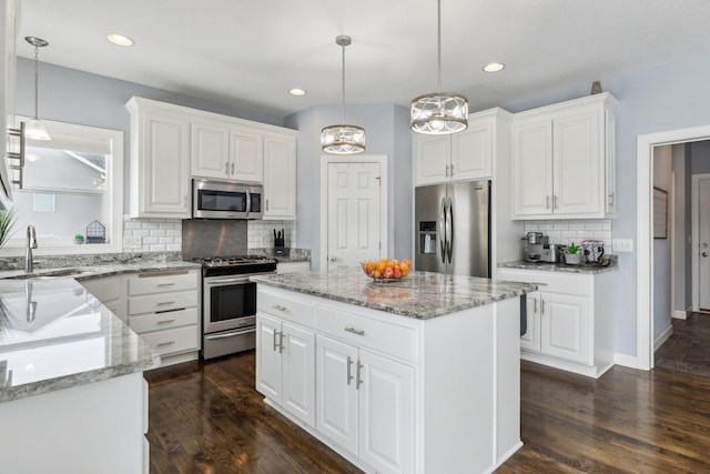 kitchen featuring white cabinetry, decorative light fixtures, a kitchen island, sink, and appliances with stainless steel finishes