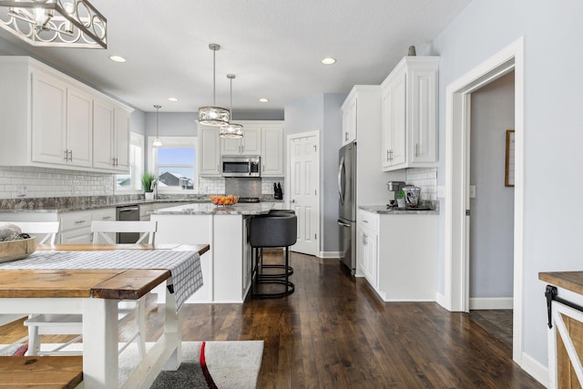 kitchen with white cabinets, a center island, stainless steel appliances, and decorative light fixtures