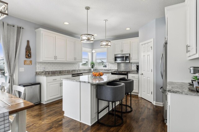 kitchen featuring appliances with stainless steel finishes, light stone countertops, pendant lighting, a center island, and white cabinetry