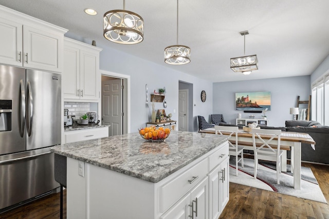 kitchen featuring a center island, white cabinetry, stainless steel fridge, hanging light fixtures, and light stone countertops