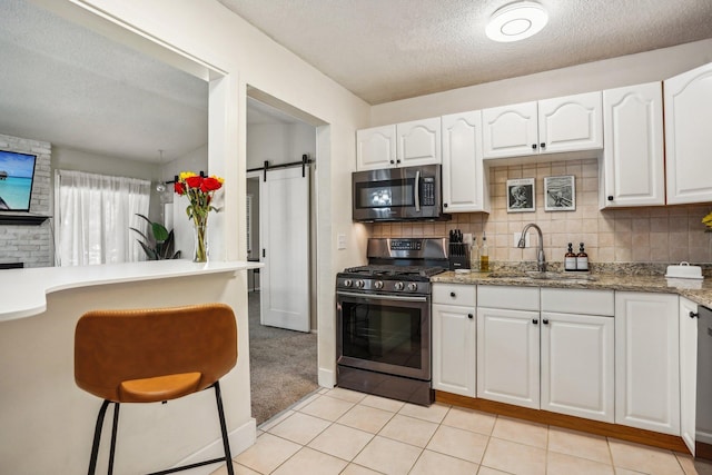 kitchen featuring sink, stone countertops, stainless steel appliances, a barn door, and white cabinets