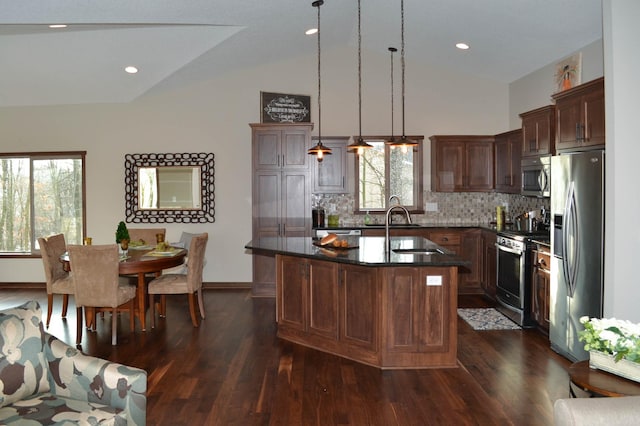 kitchen featuring hanging light fixtures, stainless steel appliances, an island with sink, backsplash, and sink