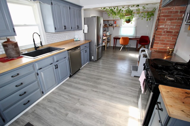 kitchen with blue cabinetry, appliances with stainless steel finishes, a sink, light wood finished floors, and backsplash