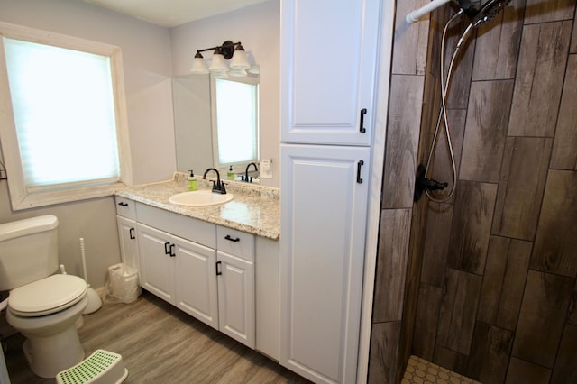 full bath with toilet, tiled shower, plenty of natural light, and wood finished floors
