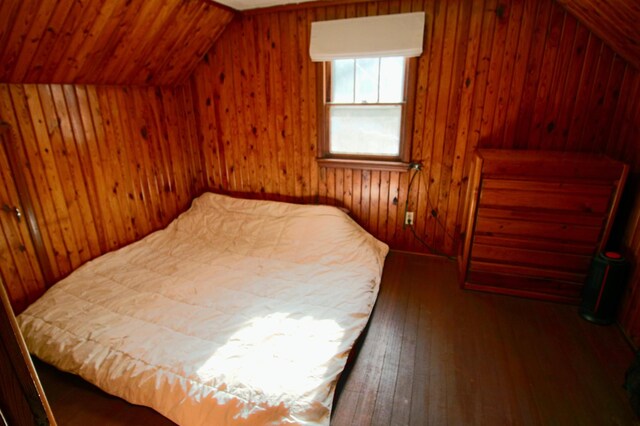 bedroom with hardwood / wood-style floors, wooden walls, and vaulted ceiling